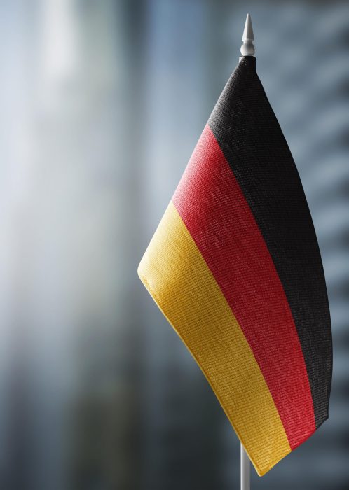 A small flag of Germany on the background of an urban abstract blurred background.